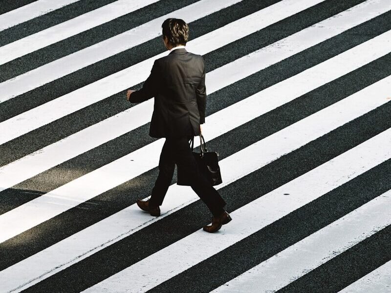 man in black formal suit jacket and pants carrying black bag while walking on pedestrian lane during daytime